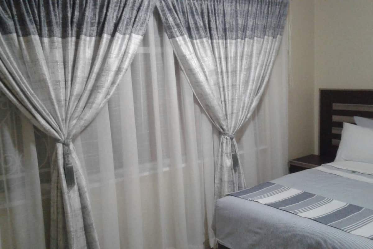 A hotel room with a bed, curtains, and a nightstand.