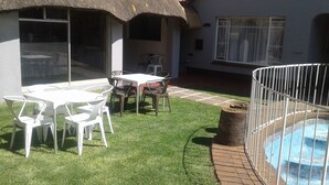 A patio with a table and chairs, a small pool, and a thatched-roof building. - Acacia Guesthouse (Kempton Park)