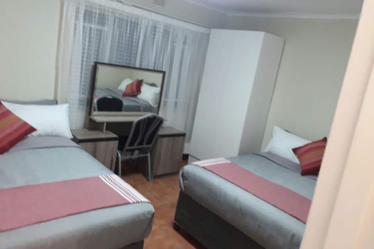 A hotel room with two beds, a desk, a chair, and a large mirror.