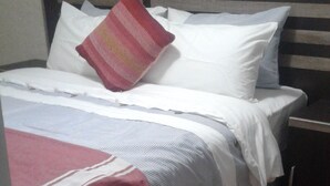 A bed with a striped bedspread, pillows, and a blanket. - Acacia Guesthouse (Kempton Park)