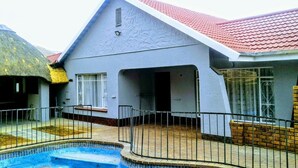 A two-story house with a swimming pool, a red-tiled roof, and a fenced yard. - Acacia Guesthouse (Kempton Park)