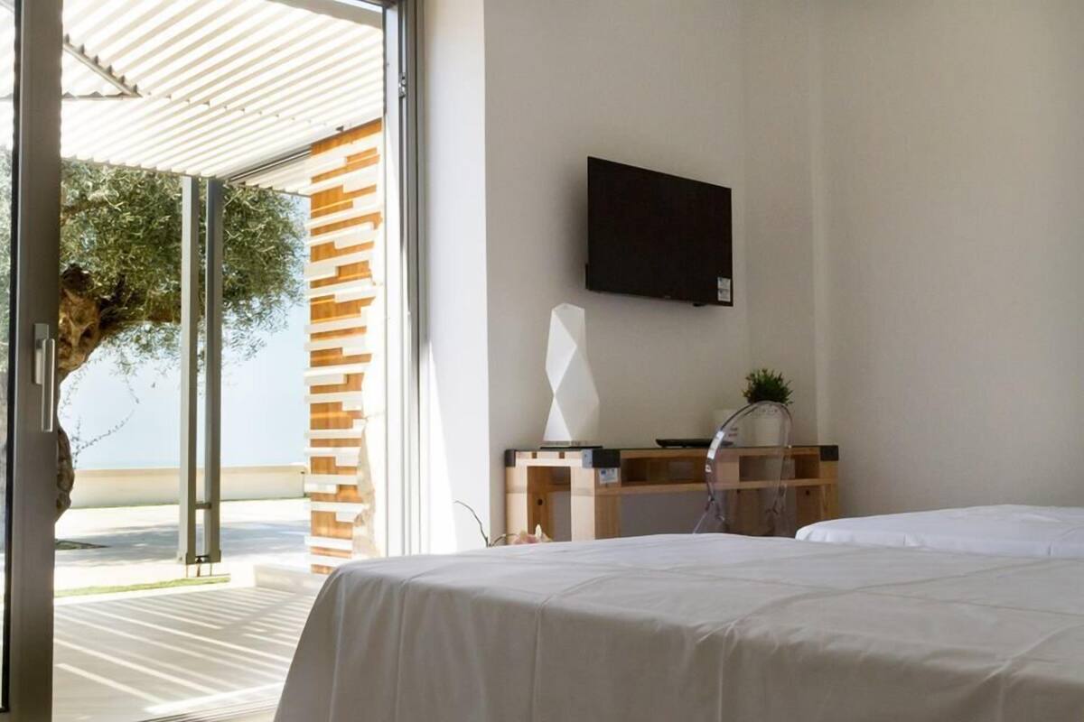 A modern hotel room with a large window, a flat-screen TV mounted on the wall, and a wooden desk with a plant.