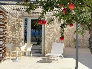 An outdoor seating area with a stone wall, a wooden pergola, and a white chair. - Daedalium Cultural Resort (Palma di Montechiaro)