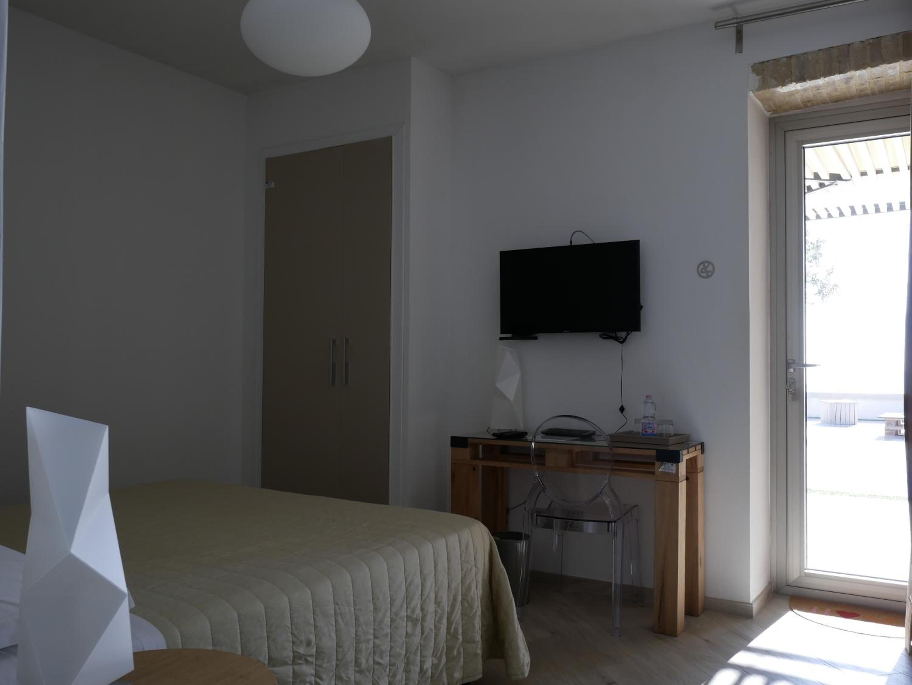 A bedroom with a bed, a desk with a chair, a television, and a sliding glass door to the outside.