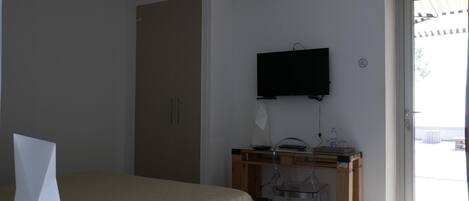 A bedroom with a bed, a desk with a chair, a television, and a sliding glass door to the outside.