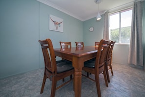 A dining room with a wooden table and chairs, a clock on the wall, and a window with curtains.