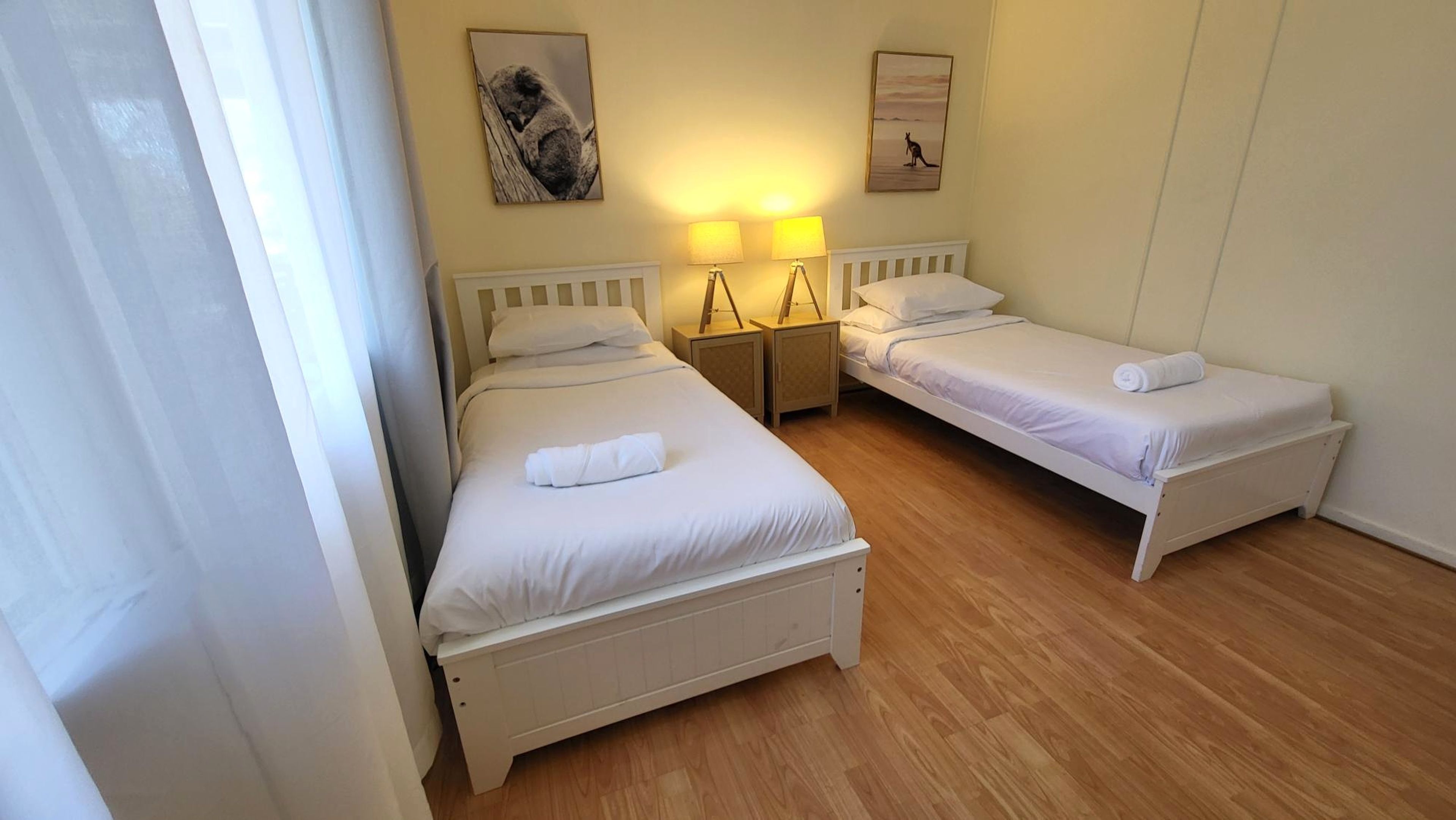 A room with two single beds, wooden flooring, and wall-mounted lamps.