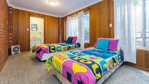 Un dormitorio con dos camas, paredes de madera, una ventana con cortinas y una puerta de baño visible.