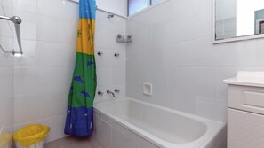 Un baño con una bañera blanca, una cortina de ducha con estampado tropical y un cubo de basura amarillo.