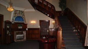 Una gran escalera con barandillas de madera y escalones alfombrados, que conduce a un rellano con chimenea y un detalle decorativo en la pared.