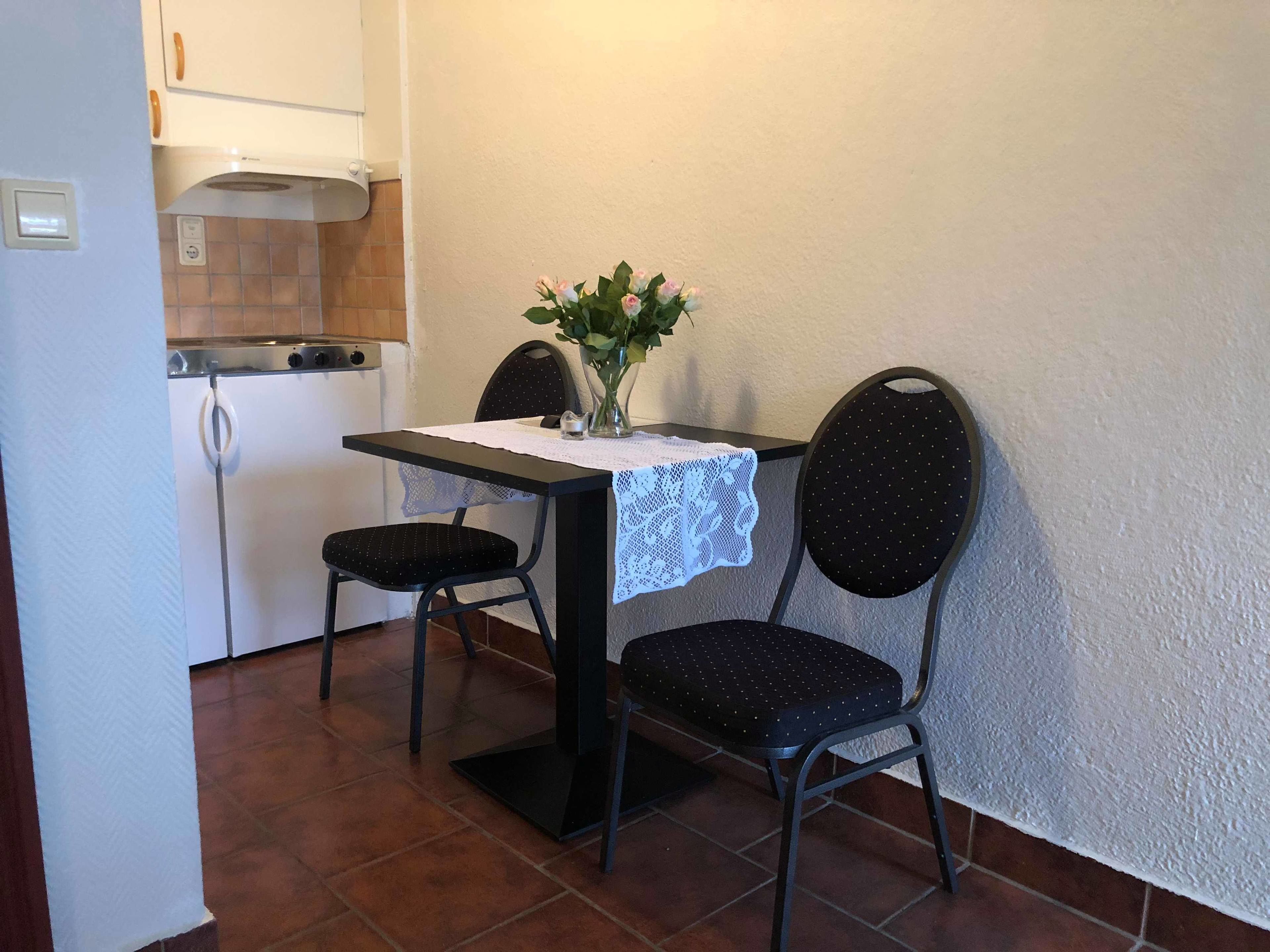 Een kleine keuken met een eettafel, twee stoelen en een vaas met bloemen.