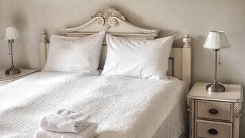 Una cama bien hecha con sábanas y almohadas blancas, una mesita de noche con una lámpara y dos cuadros en la pared.