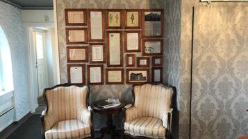 Una habitación con dos sillones tapizados, una mesita redonda y una pared decorada con documentos enmarcados.