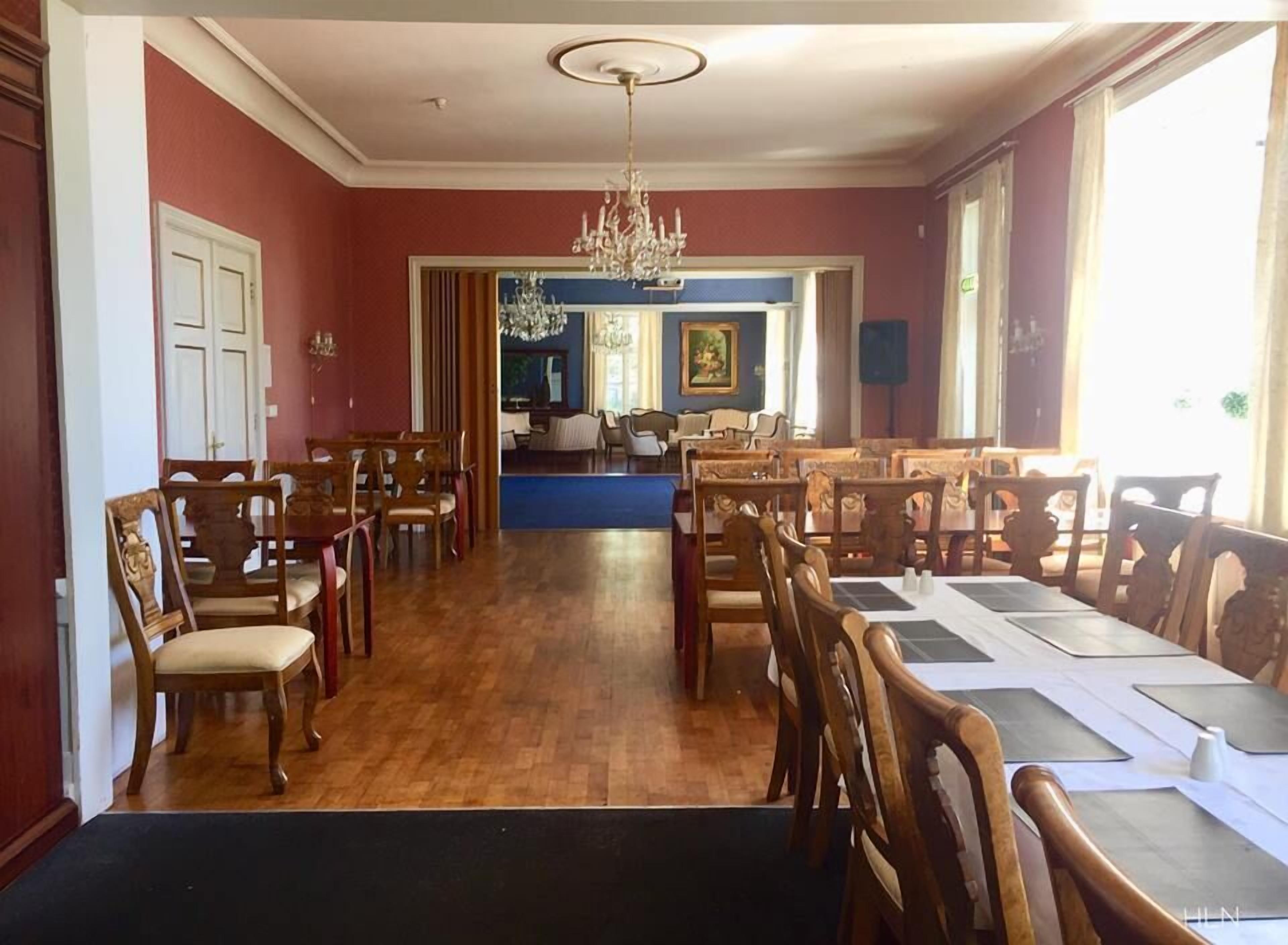 Un comedor con sillas y mesas de madera, una araña y vistas a un salón con una pared azul de acento.