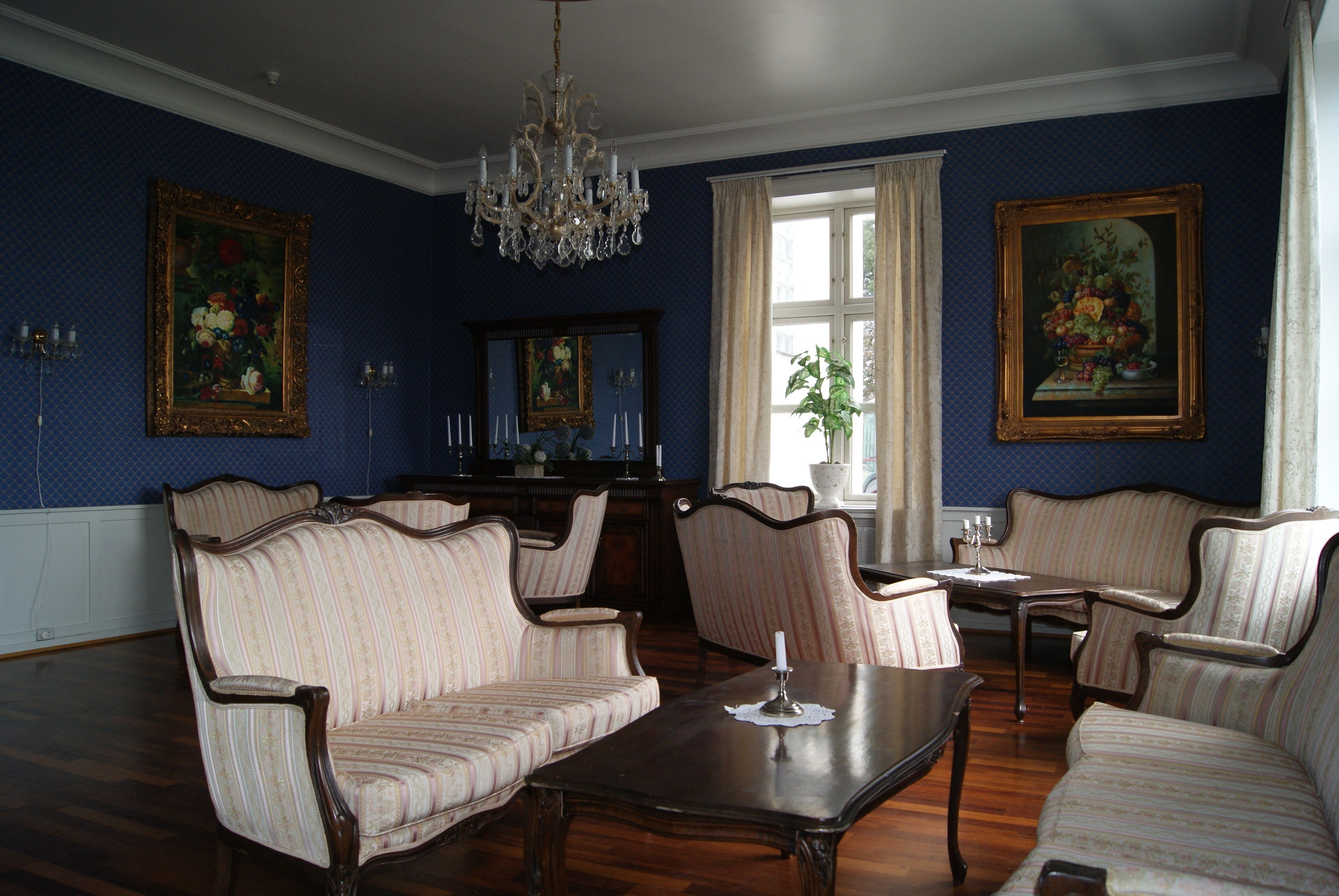 Una habitación con candelabro, sofás estampados, una mesa de madera y cuadros enmarcados en las paredes.
