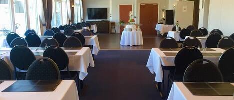 Un salón de conferencias con mesas, sillas, una pantalla grande y candelabros.