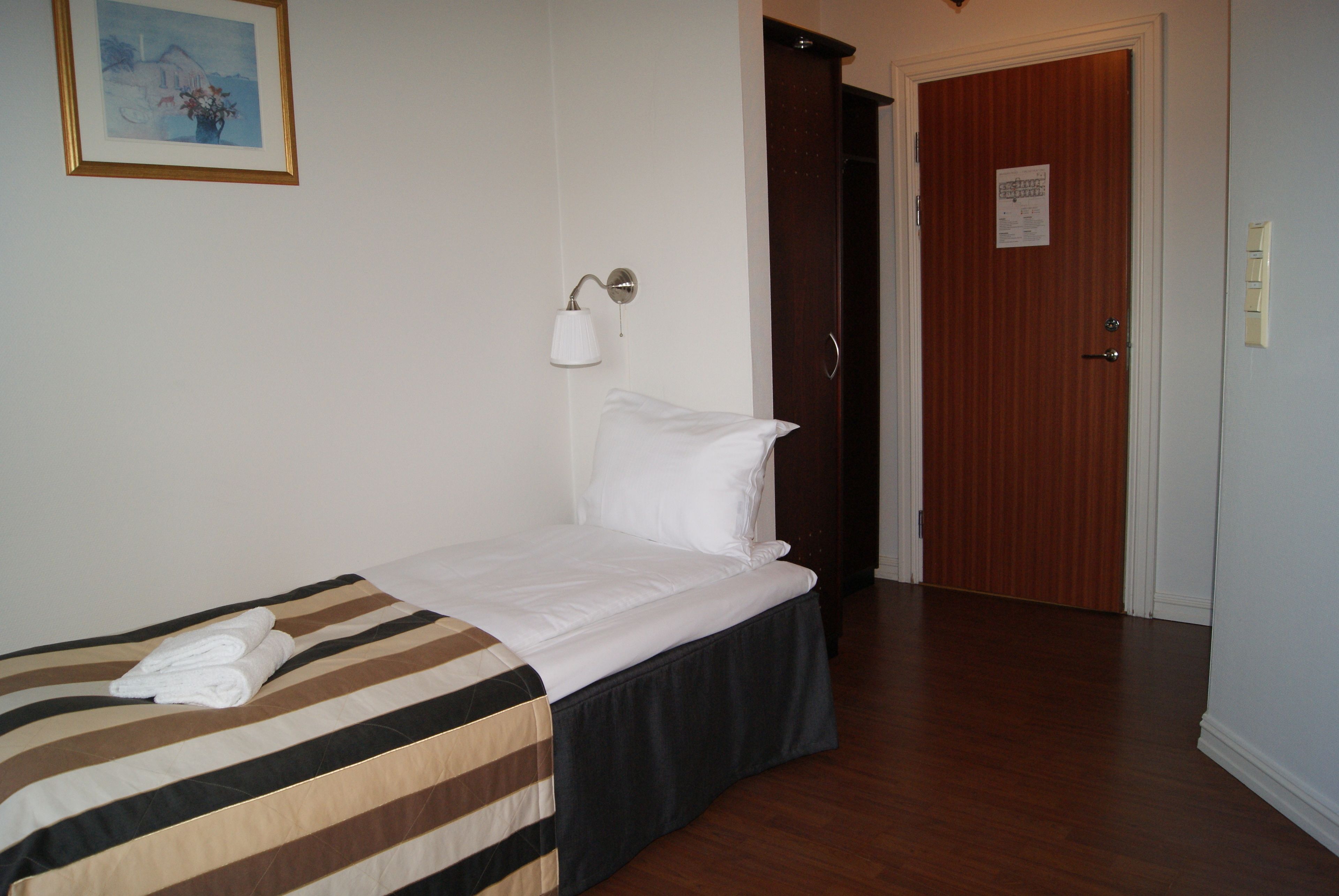 Ett hotellrum med en säng, en sänglampa, en dörr och en inramad tavla på väggen.