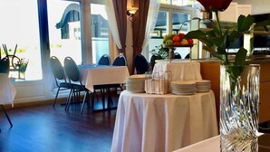 Un comedor con mesas dispuestas para el servicio, una araña de cristal y un jarrón con una rosa.