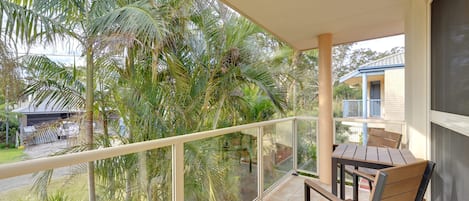 Ein Balkon mit Tisch und Stühlen, der auf einen Wohnbereich mit Palmen und einem Haus blickt.