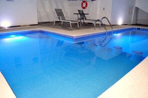 A swimming pool with a tiled edge, a lifebuoy on the wall, and lounge chairs.