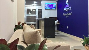 Un área de recepción con pared azul, mostrador de recepción, candelabro y pantalla de televisión.
