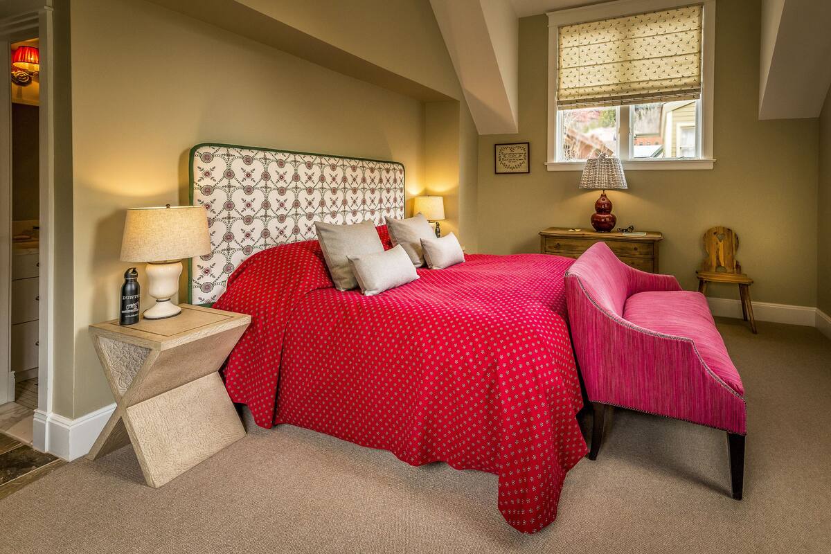 A bedroom with a large bed, a nightstand, a chair, and a window with a view.