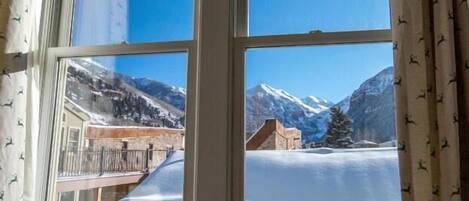Ein Fenster mit freiem Blick auf eine verschneite Berglandschaft, darunter ein Gebäude mit einem Balkon.