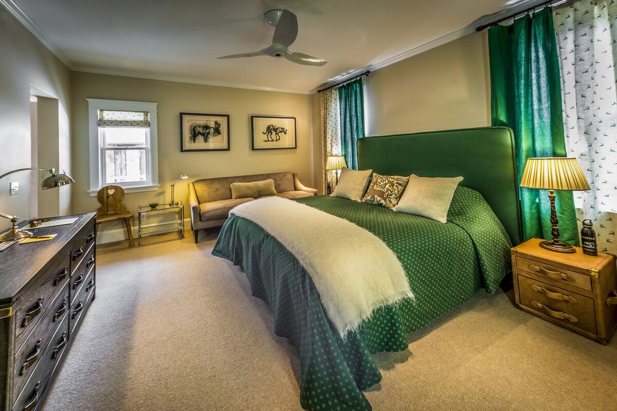 A bedroom with a large bed, a desk, a chair, a lamp, and a ceiling fan.
