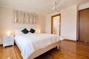 Een slaapkamer met een bed, nachtkastjes, een plafondventilator, een houten vloer en een deur.
