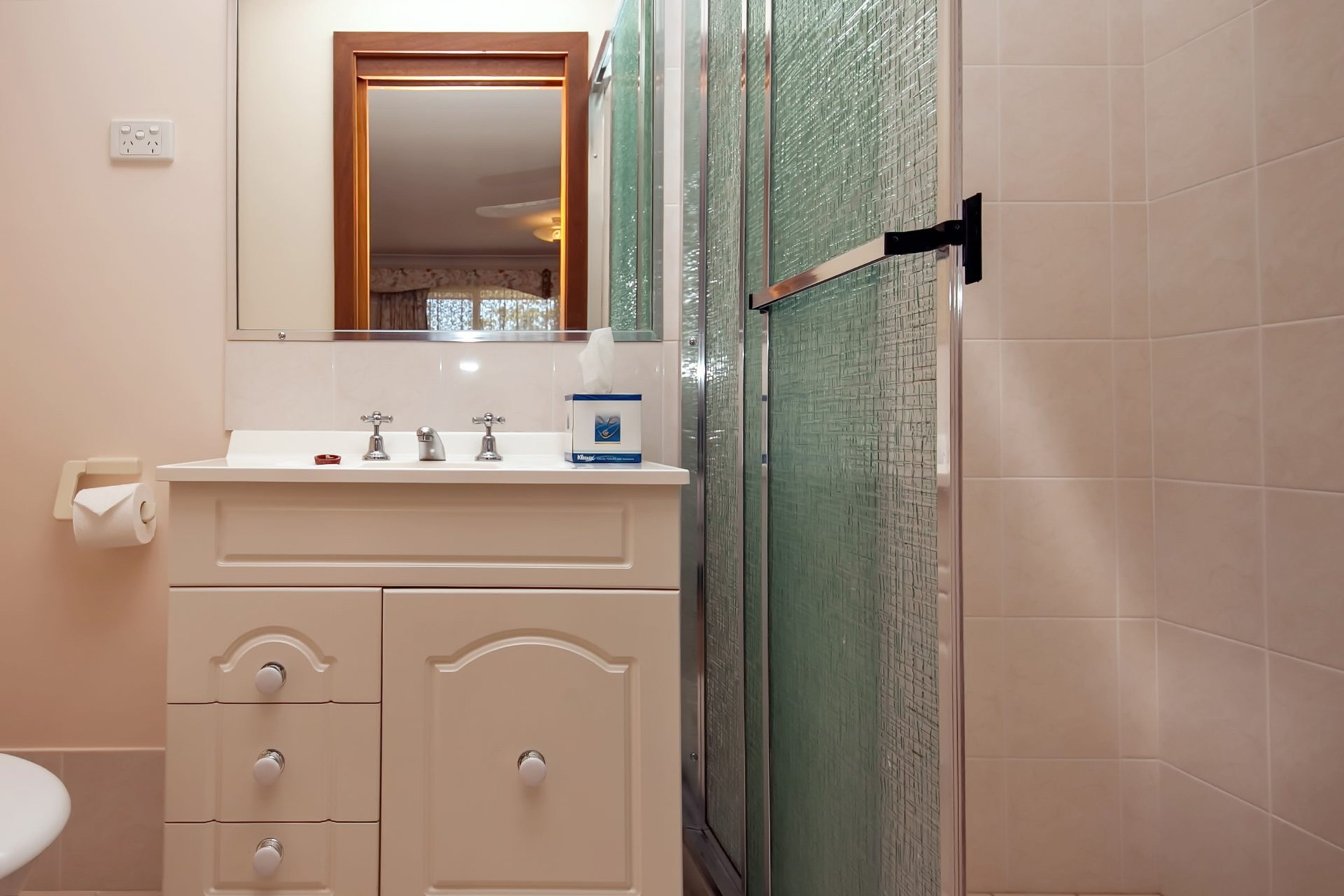 A bathroom with a white sink, a mirror, a towel dispenser, and a glass shower enclosure.