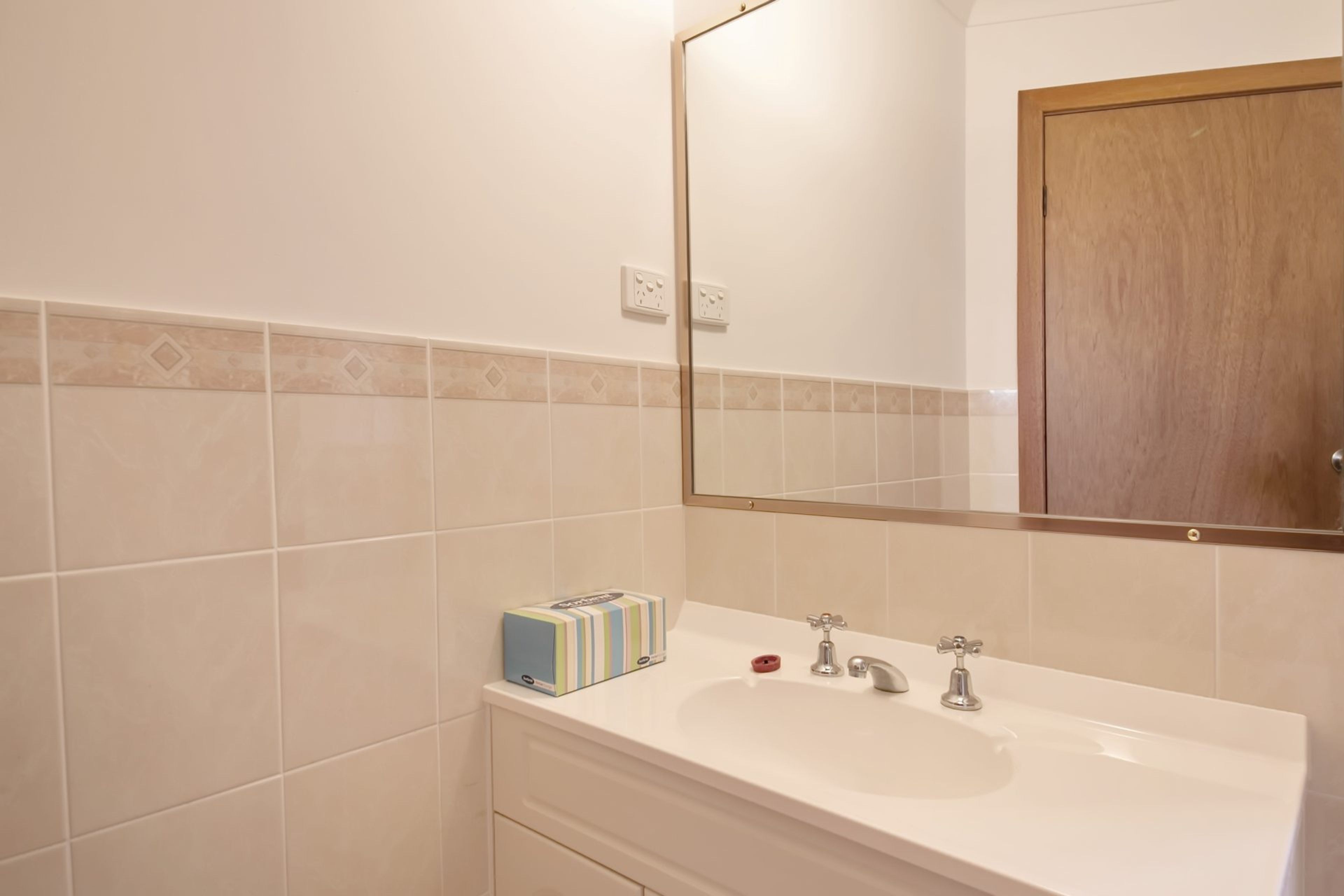 A bathroom with a white sink, two faucets, a mirror, and a wooden door.