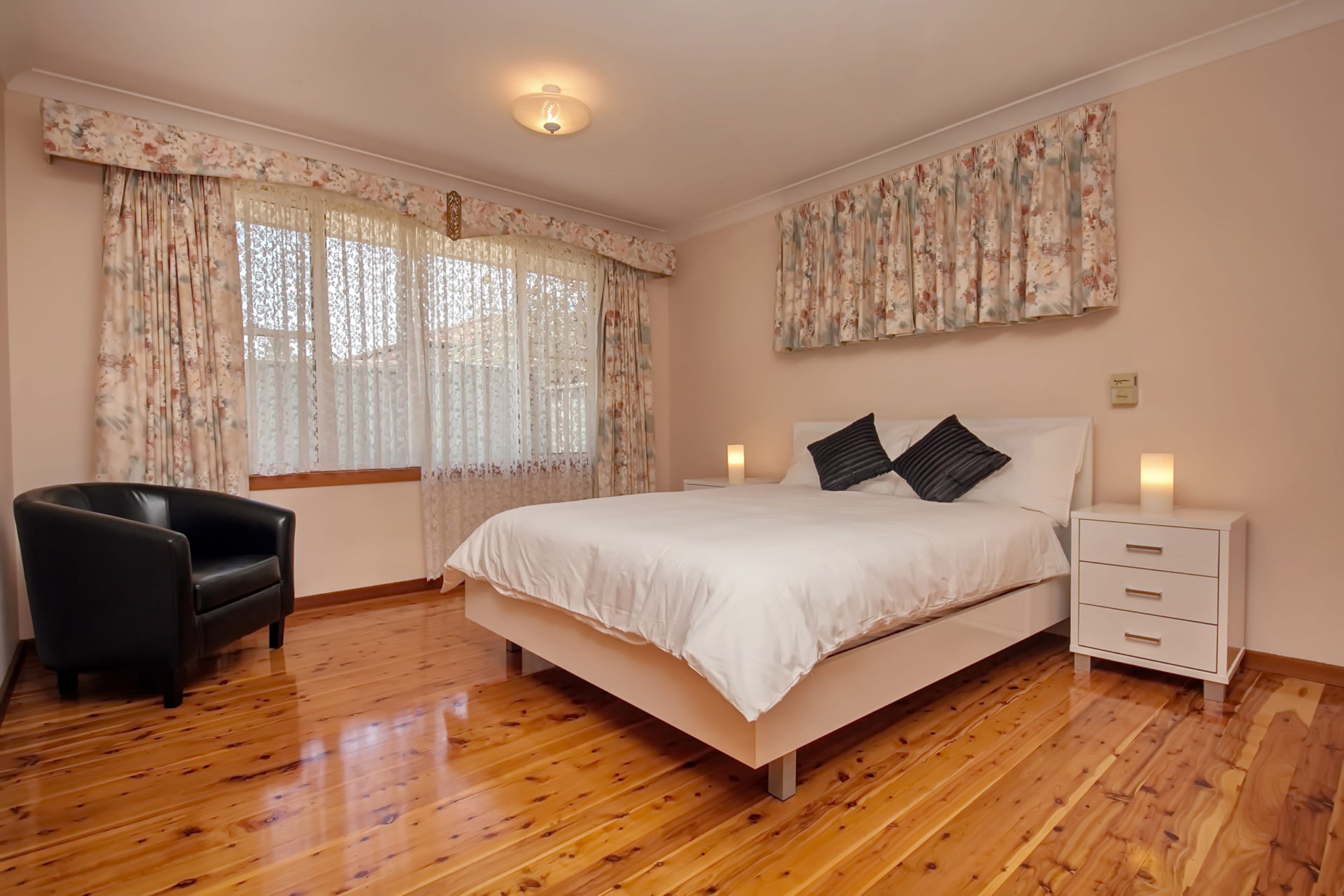 A bedroom with a bed, a chair, a nightstand, and a window with curtains.