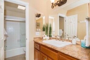 A bathroom with a white bathtub, a sink with a mirror above it, and a vanity with a countertop. - Pier View Escape (Oceanside)