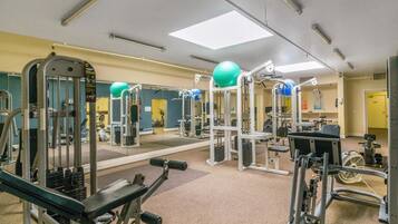 Ein Fitnessstudio mit verschiedenen Trainingsgeräten, Spiegeln und einem Deckenventilator.