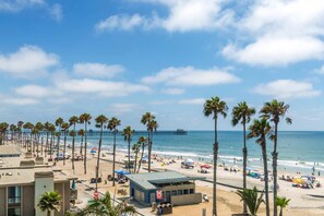 A beach with palm trees, a pier, and a building with a blue roof. - Pier View Escape (Oceanside)