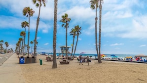 Une plage bordée de palmiers, avec une tour de surveillance pour les sauveteurs, des tables de pique-nique et des parasols.