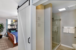 A bedroom with a bed, a wardrobe, and a glass shower enclosure. - Our Ocean View (Oceanside)