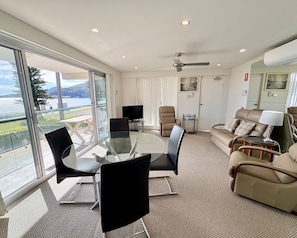 Sala de estar moderna com mesa de vidro, assentos confortáveis, TV de tela plana e vista para um lago.