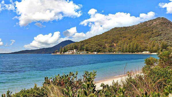 A coastal landscape with a clear view of a beach, a mountain in the background, and a few buildings along the shore.