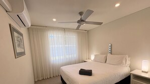 Een hotelkamer met een bed, een plafondventilator, een nachtkastje met een lamp en een raam met gordijnen.