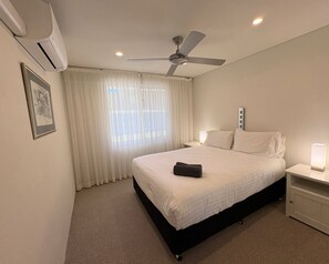 Quarto de hotel com cama, ventoinha no teto, mesa de cabeceira com abajur e janela com cortinas.