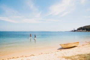 A beach with clear water, a boat on the shore, and a distant shoreline with buildings.