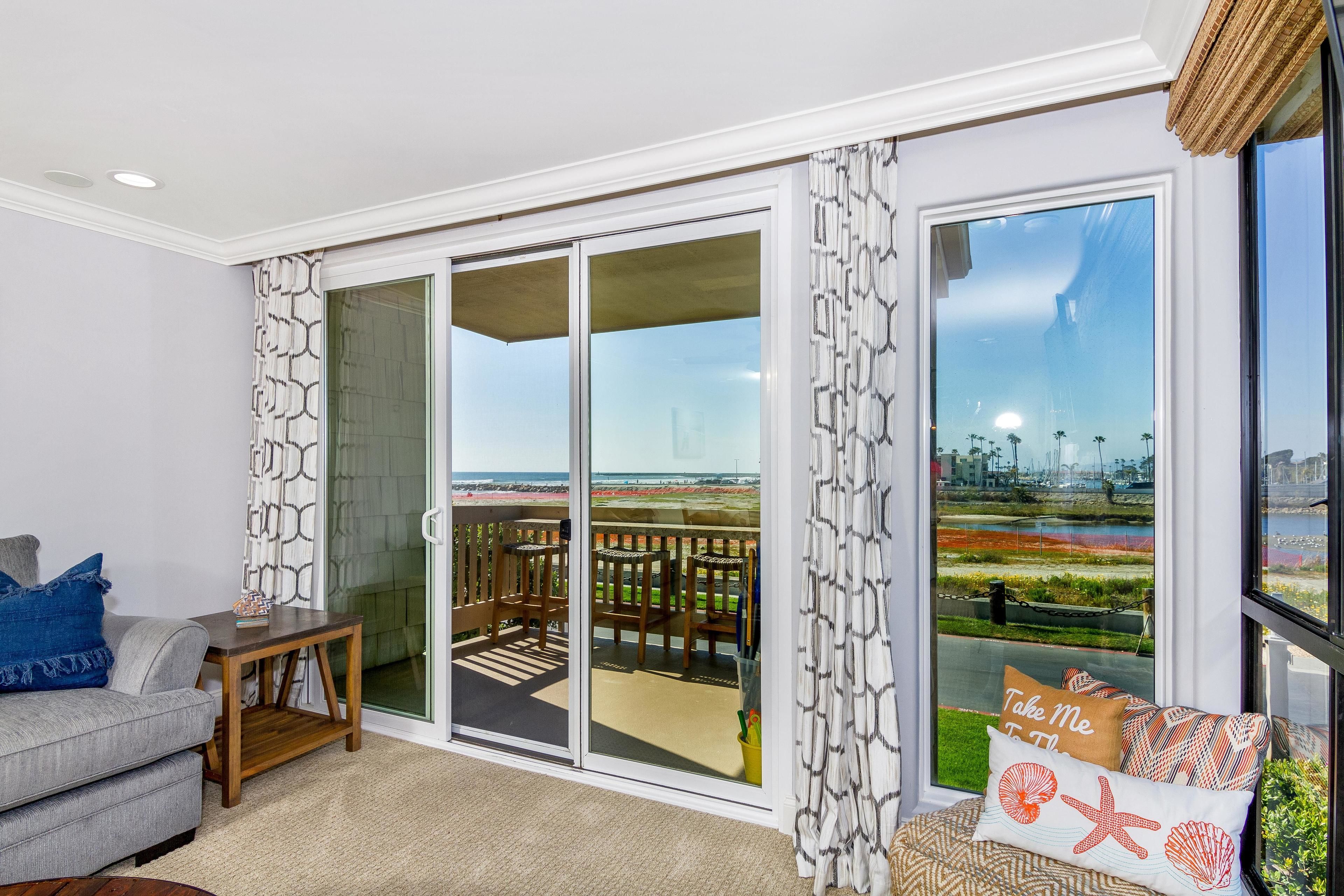 Sala de estar com porta de vidro deslizante que dá para uma varanda com vista para uma área ajardinada e um horizonte urbano ao longe.