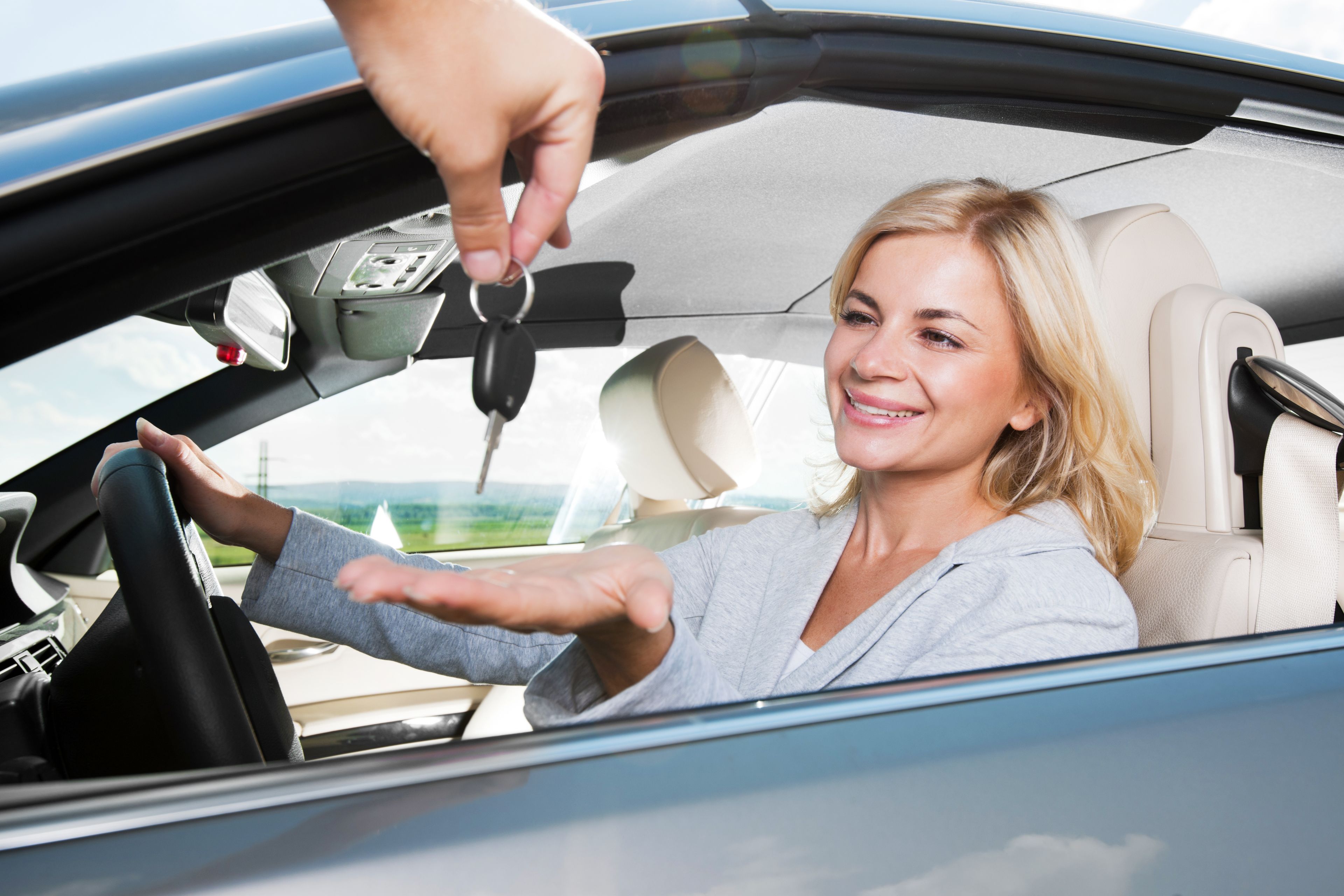 A person handing over car keys to another person inside a car.