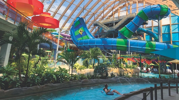 Un parc aquatique intérieur doté d’un grand toboggan aquatique, d’un espace piscine et d’une structure avec un toit en verre.