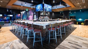 Un espace bar doté d’un îlot central, de nombreux tabourets de bar et d’un grand écran diffusant du contenu.
