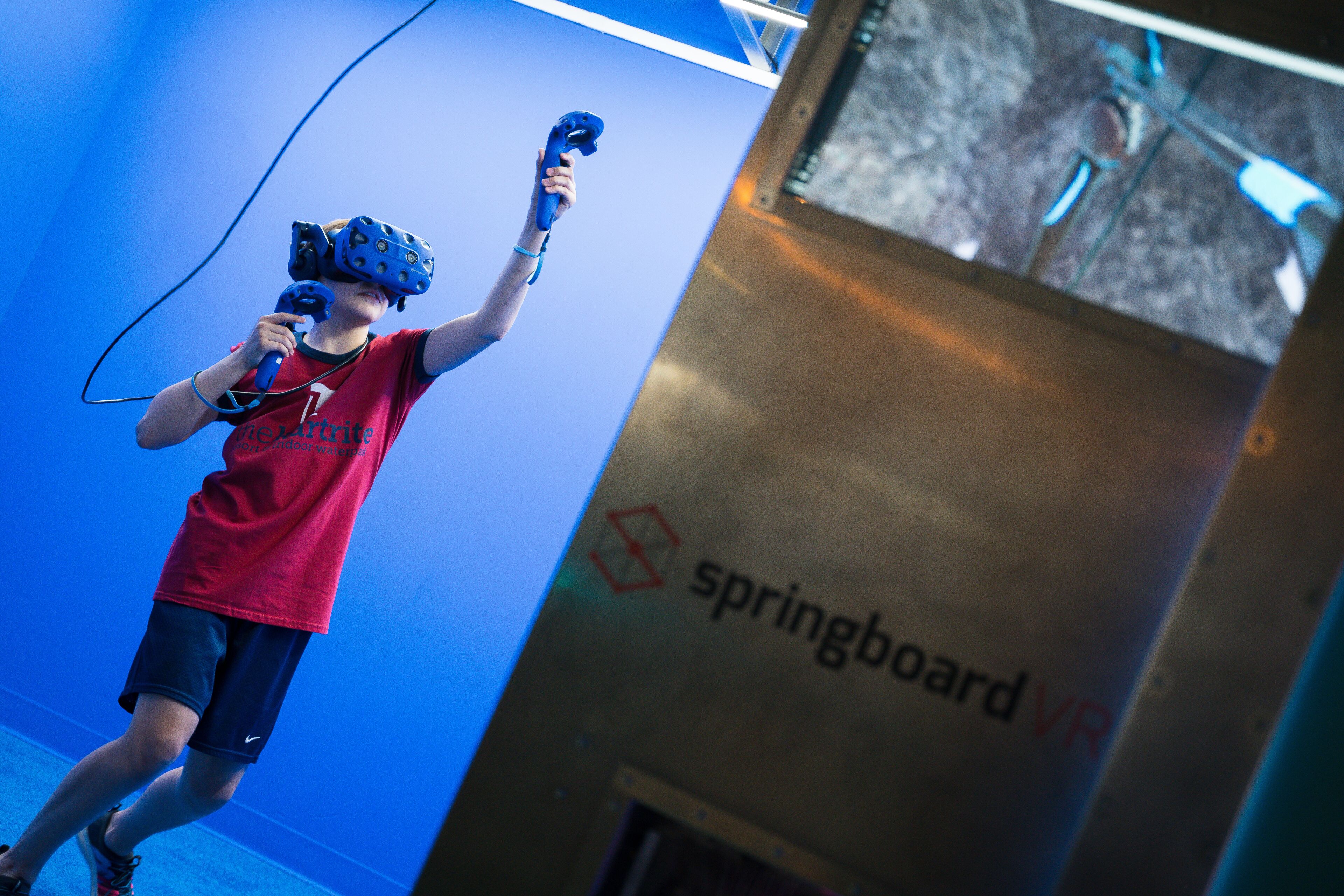 A person wearing a VR headset and holding a VR controller in a room with a blue wall and a sign that reads "springboard VR".