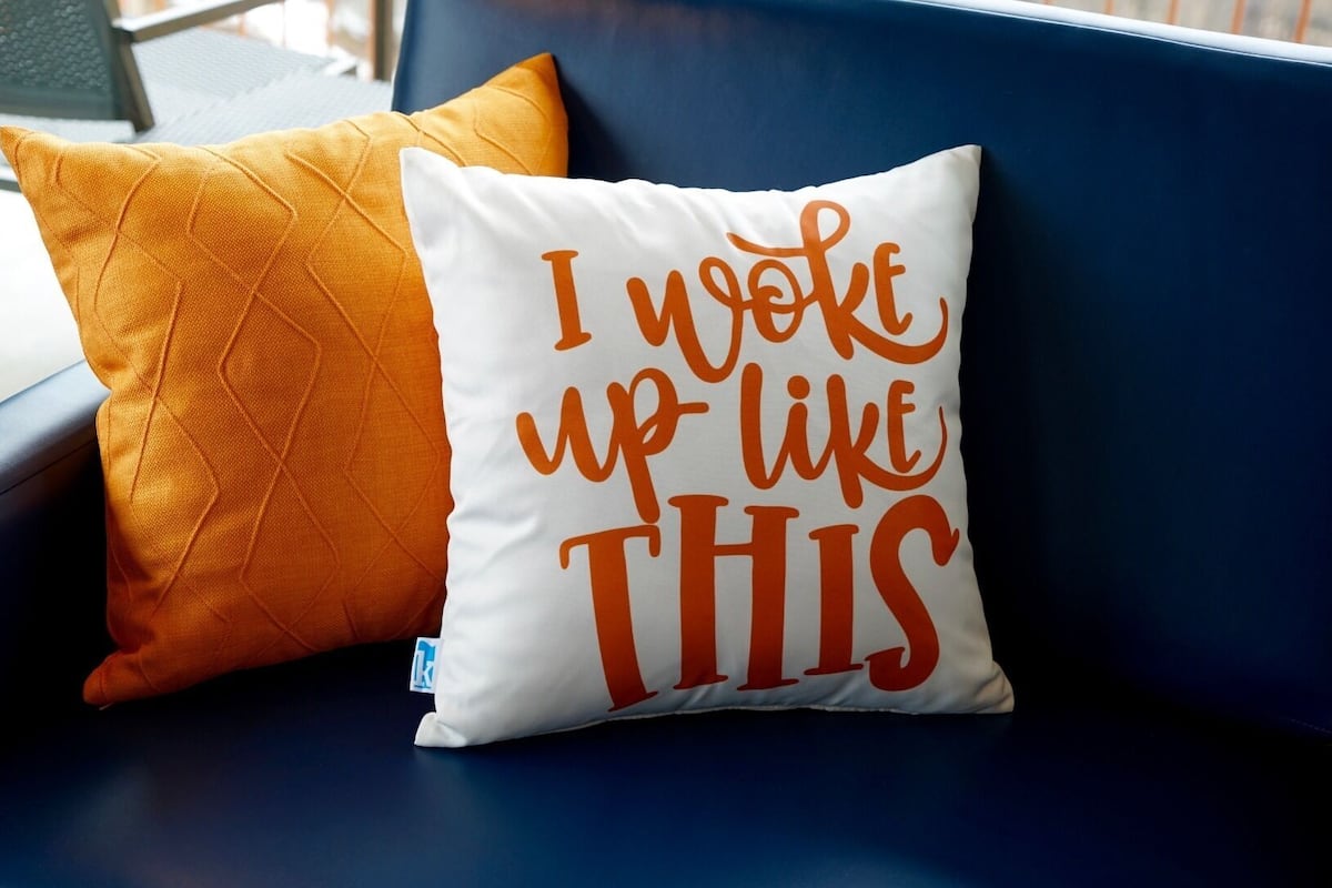 Un sofá azul con dos almohadones, uno naranja y otro blanco con texto.