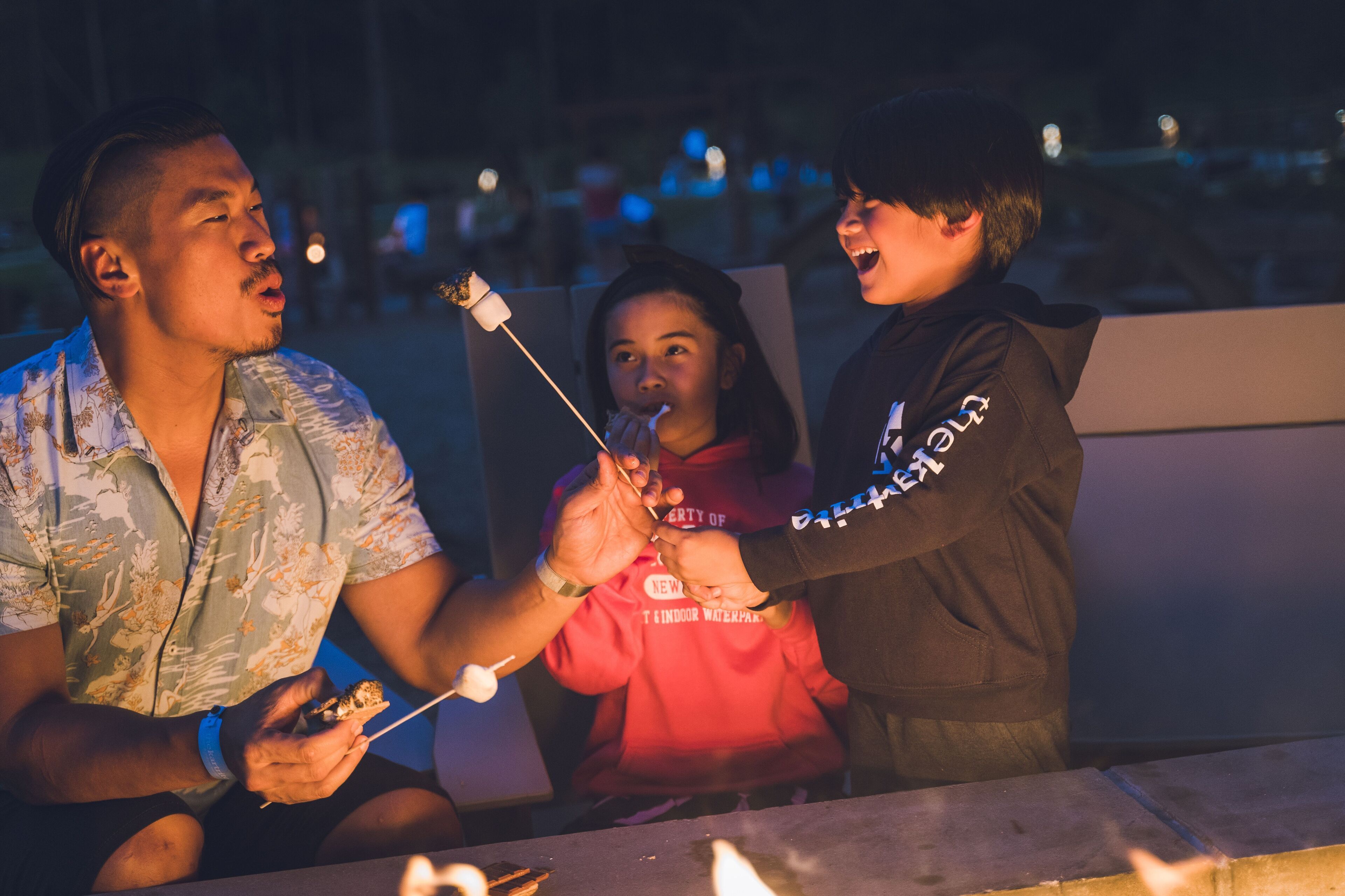 Tre persone che arrostiscono marshmallow attorno a un fuoco da campo.