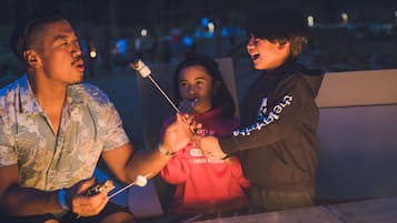 Three people roasting marshmallows around a campfire.